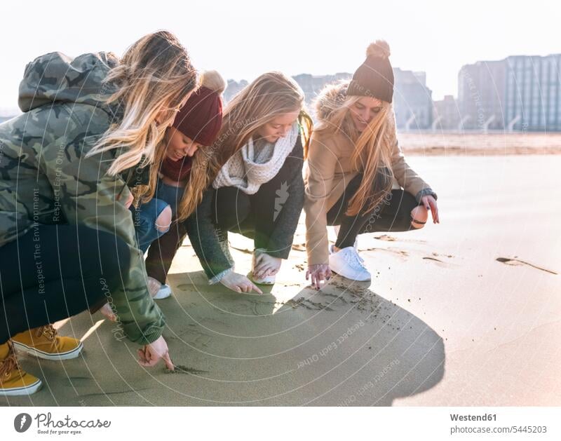 Four friends drawing in the sand on the beach mate female friend beaches cower cowering crouch sandy scratch sketch sketching human human being human beings
