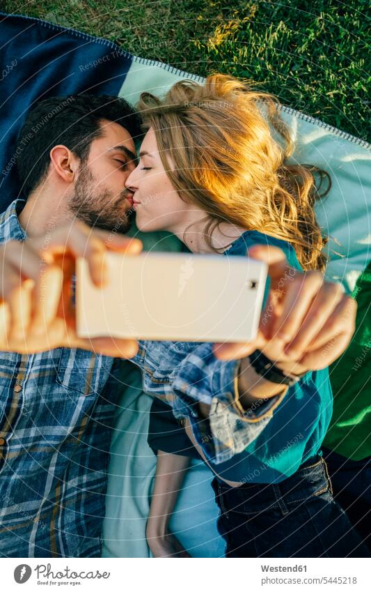 Couple in love taking selfie with smartphone while kissing kisses Selfie Selfies meadow meadows photographing couple twosomes partnership couples lying