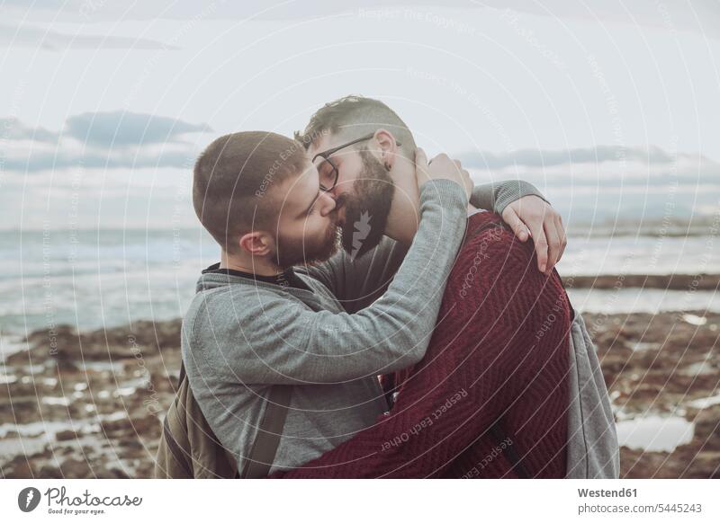 Young gay couple hugging and kissing in front of the sea twosomes partnership couples beach beaches kisses people persons human being humans human beings