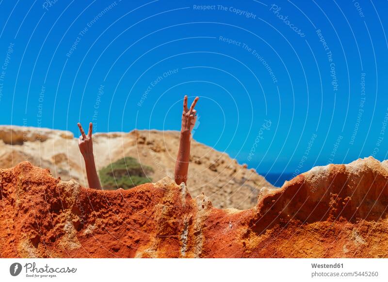 Woman doing victory sign behind rock at the beach rocks sky skies Travel leisure free time leisure time hidden Quality Time Portugal Humour Humorous