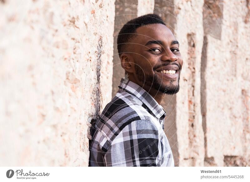 Portrait of smiling young man leaning against wall portrait portraits men males Adults grown-ups grownups adult people persons human being humans human beings