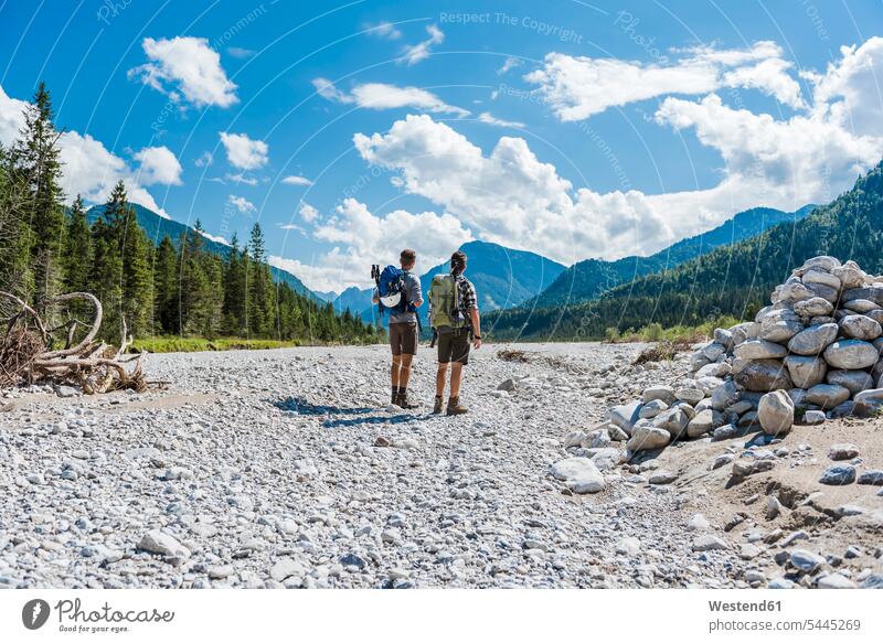 Germany, Bavaria, back view of two hikers standing in dry creek bed looking at view friends wanderers friendship hiking watching river bed riverbed backpack
