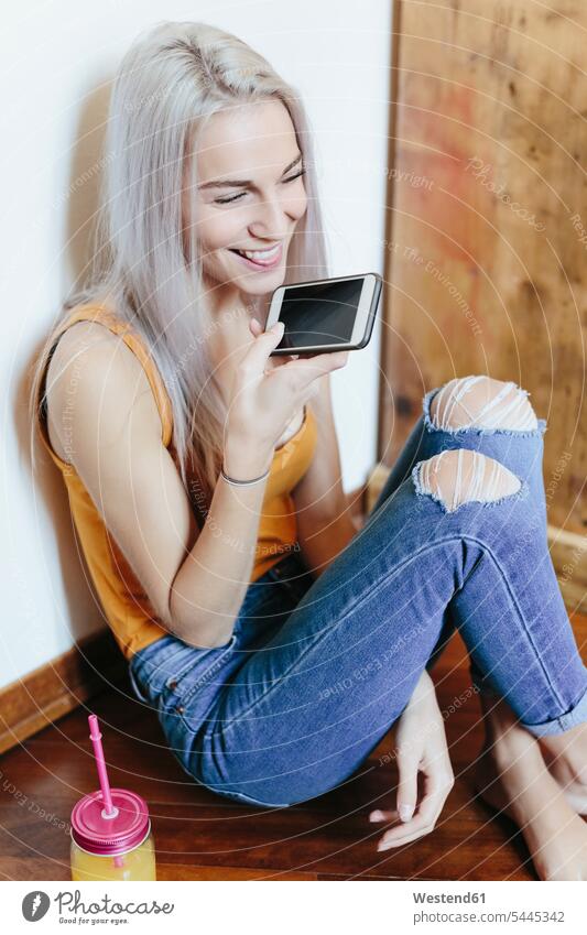 Happy young woman sitting on the floor at home using smartphone happiness happy floors females women Smartphone iPhone Smartphones Seated use Adults grown-ups