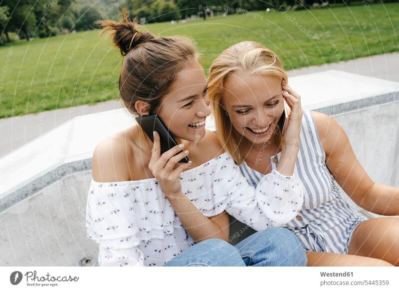 Two happy young women with cell phones in a skatepark female friends woman females happiness parks Skateboard Park skate park on the phone call telephoning