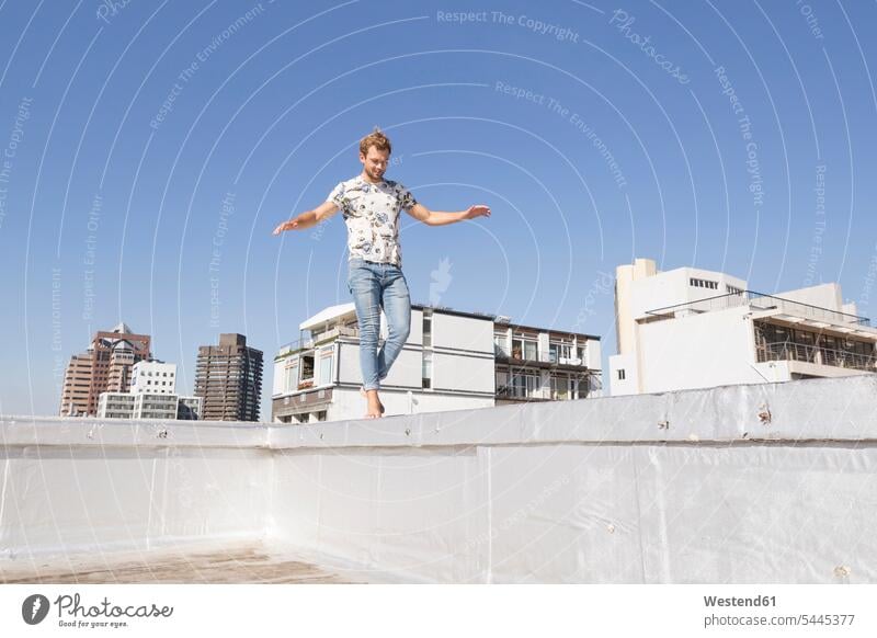 Barefooted man balancing on balustrade of a rooftop terrace balance parapet roof terrace deck blond blond hair blonde hair happiness happy carefree men males