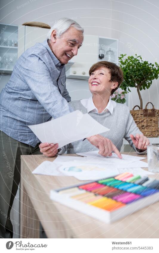 senior woman painting with crayons, husband watching drawing sketching senior adults seniors old smiling smile together pointing point at pointing at show