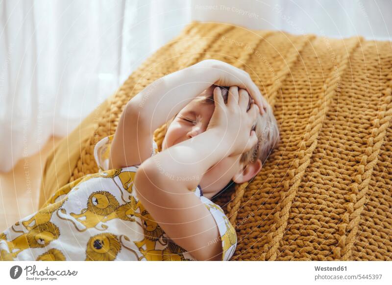 Little boy lying on cushion covering face with his hands boys males child children kid kids people persons human being humans human beings laying down lie