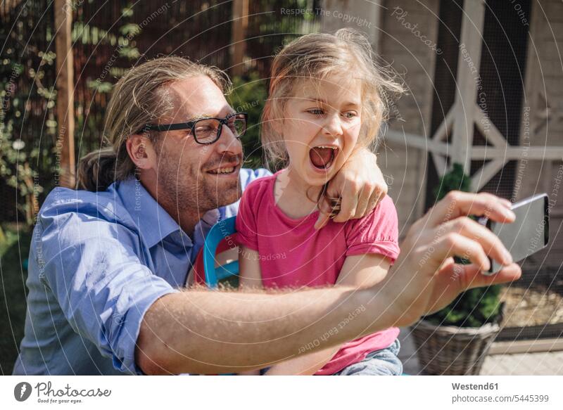 Father and daughter taking a selfie in garden mobile phone mobiles mobile phones Cellphone cell phone cell phones father pa fathers daddy dads papa Selfie