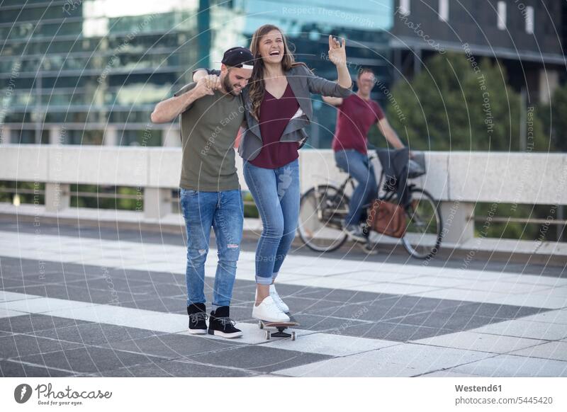 Young man supporting laughing girlfriend on skateboard Fun having fun funny couple twosomes partnership couples Laughter people persons human being humans