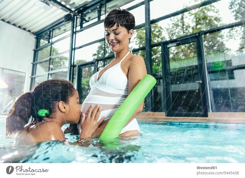 Girl kissing belly of her pregnant mother in indoor swimming pool indoor swimming pools mommy mothers ma mummy mama bellies abdomen human abdomen swimming bath