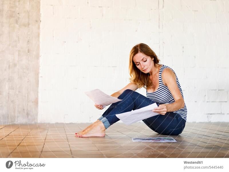 Woman sitting on the floor reviewing paper woman females women floors Seated Adults grown-ups grownups adult people persons human being humans human beings