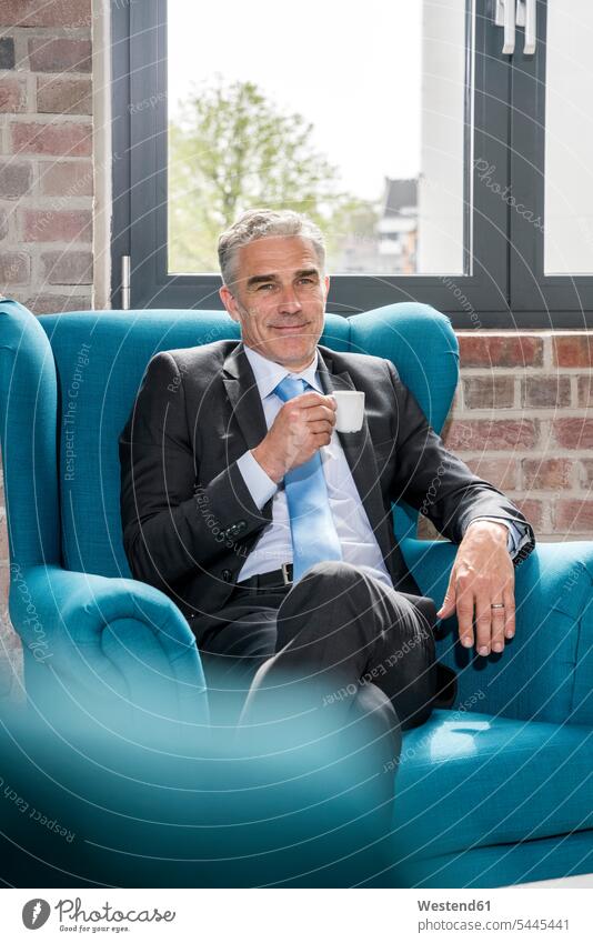Mature businessman sitting in arm chair, drinking coffee Seated armchair Arm Chairs armchairs Coffee Businessman Business man Businessmen Business men office