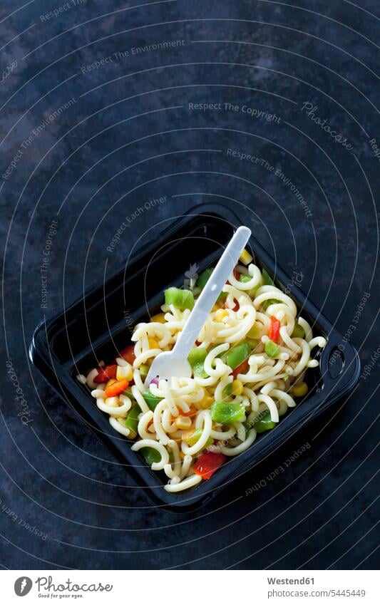 Plastic box of noodle salad with corn and bell pepper on dark ground garnished maize ready to eat ready-to-eat plastic bowl plastic bowls take away