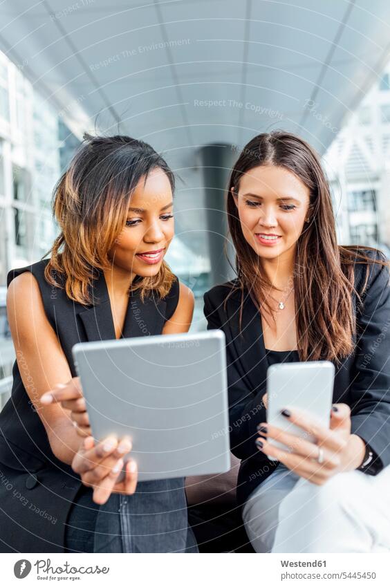 Two businesswomen working with smartphone and tablet in the city businesswoman business woman business women females Female Colleague mobile phone mobiles