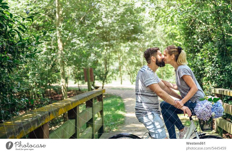 Couple with bicycle kissing on a wooden walkway in the countryside bikes bicycles path trail paths couple twosomes partnership couples rural kisses people