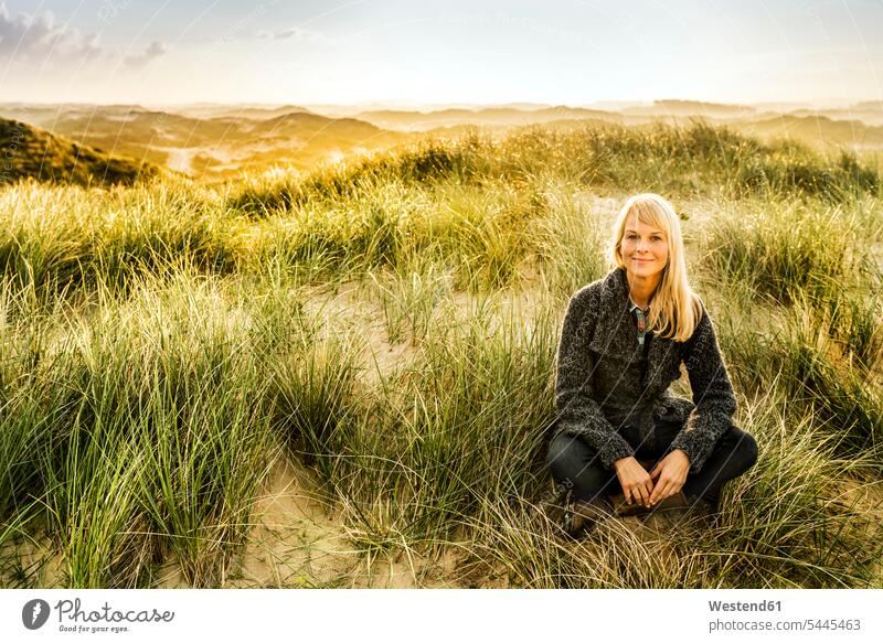 Portrait of smiling woman sitting in dunes beach beaches females women sand dune sand dunes Seated smile Adults grown-ups grownups adult people persons