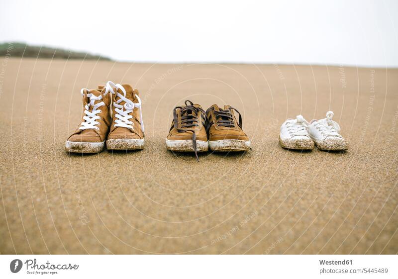 Three pairs of shoes with different sizes on the beach sand sandy beaches Size Difference close-up close up closeups close ups close-ups side by side paralell