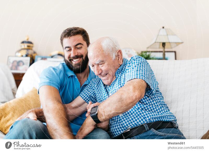 Adult grandson and his grandfather sitting on the couch at home tickling each other grandsons tickle grandpas granddads grandfathers grandchild grandchildren