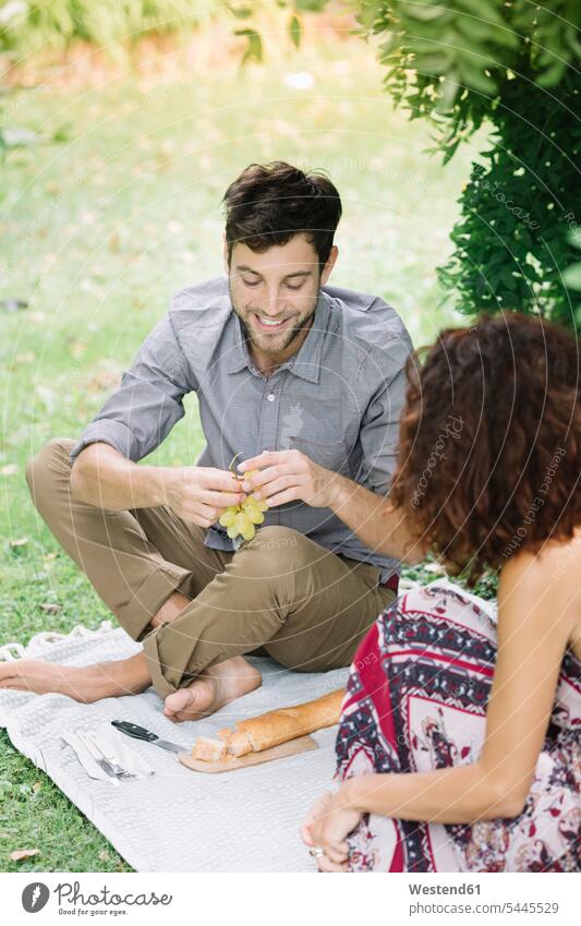 Happy couple having a picnic in a park twosomes partnership couples Picnic picnicking parks smiling smile people persons human being humans human beings Meals