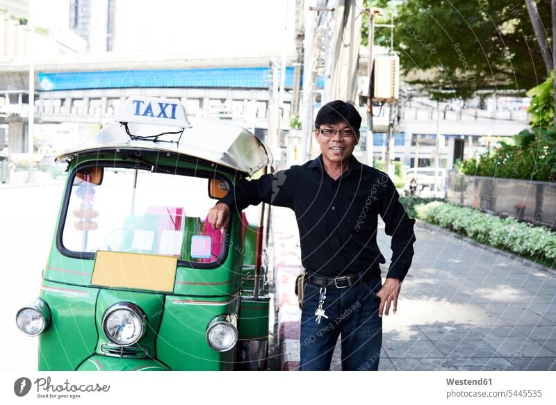 Thailand, Bangkok, tuk tuk driver standing next to his vehicle on the street streets City Street City Streets three-quarter length three quarter length writing