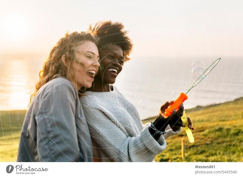 Two best friends making soap bubbles outdoors at sunset female friends happiness happy woman females women mate friendship Adults grown-ups grownups adult