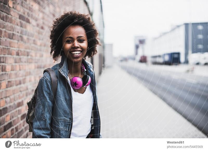 Portrait of smiling young woman with headphones and backpack standing on pavement females women portrait portraits Adults grown-ups grownups adult people