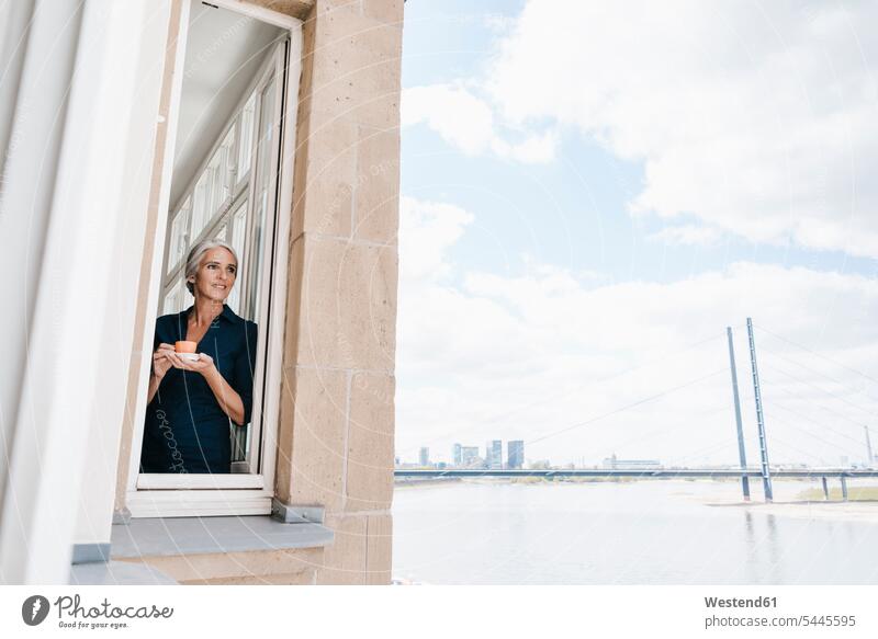 Businesswoman looking out of window in waterfront office Coffee females women smiling smile businesswoman businesswomen business woman business women windows