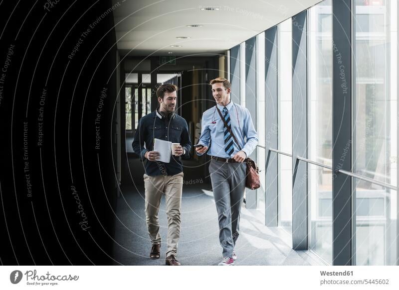 Two colleagues walking and talking on office floor speaking Businessman Business man Businessmen Business men offices office room office rooms mobile phone
