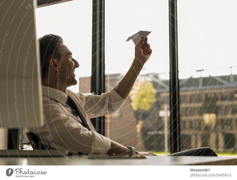 Businessman sitting at desk in his office looking at paper plane Business man Businessmen Business men paper dart paper planes paper darts paper aeroplane