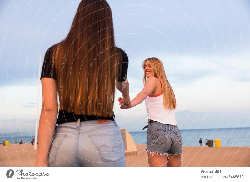 Two happy young women hand in hand on the beach beaches female friends woman females mate friendship Adults grown-ups grownups adult people persons human being