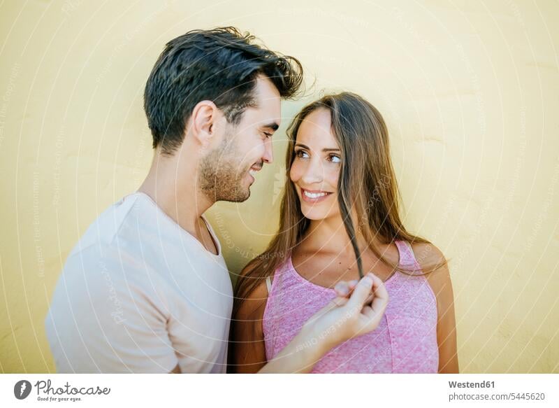 Young couple looking at each other in love against yellow wall eyeing happiness happy twosomes partnership couples smiling smile view seeing viewing people
