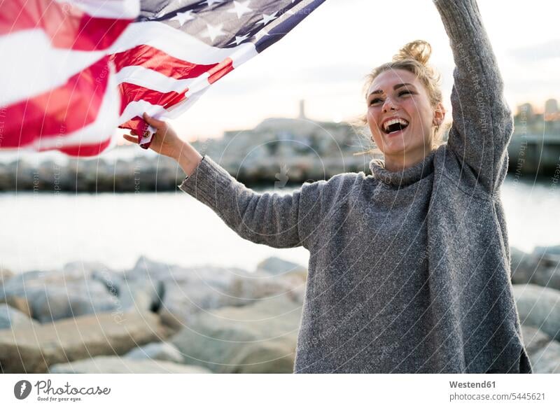 Portrait of laughing young woman holdding blowing US American flag females women American Flag American Flags Flag of America Laughter Adults grown-ups grownups