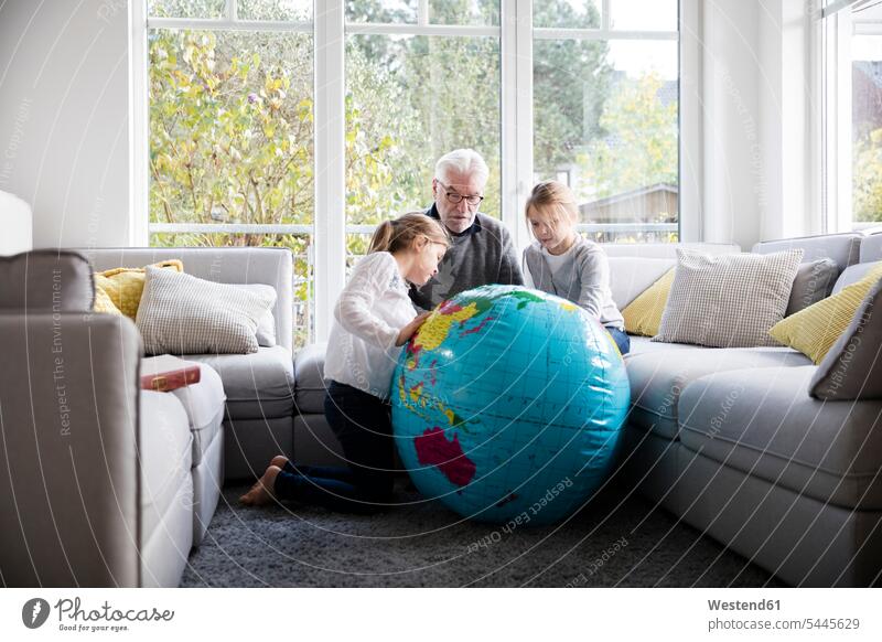 Two girls and grandfather with globe in living room females living rooms livingroom grandpas granddads grandfathers globes child children kid kids people