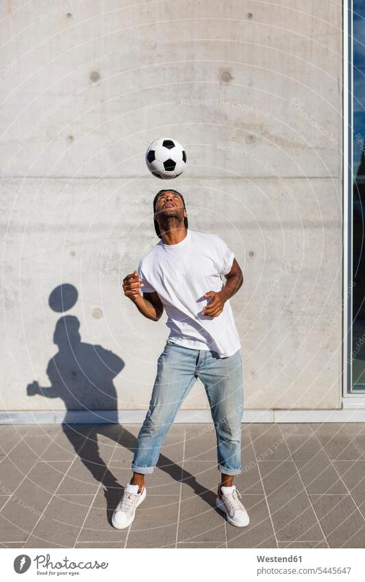 Young man playing with soccer ball in front of concrete wall soccer balls footballs men males Adults grown-ups grownups adult people persons human being humans