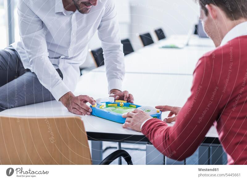 Two colleagues in office playing foosball offices office room office rooms table football table soccer Businessman Business man Businessmen Business men