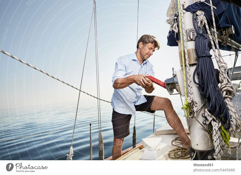 Mature man working on his sailing boat men males Adults grown-ups grownups adult people persons human being humans human beings boat sports standing crank