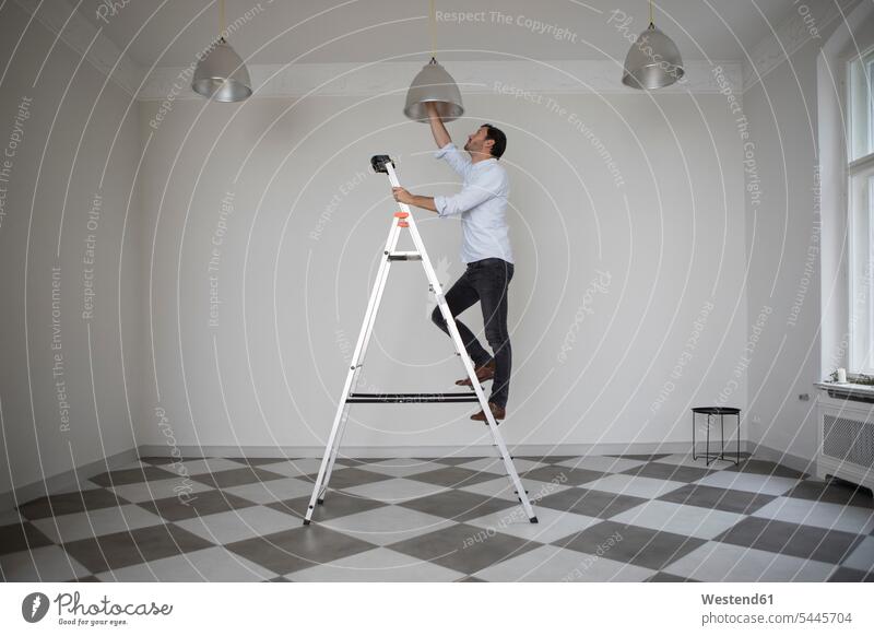 Man standing on ladder in an empty room changing bulb of ceiling light man men males Adults grown-ups grownups adult people persons human being humans