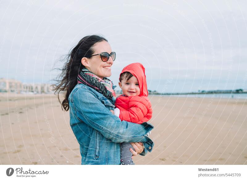 Portrait of smiling baby girl on her mother's arms on the beach baby girls female mommy mothers mummy mama infants nurselings babies beaches people persons