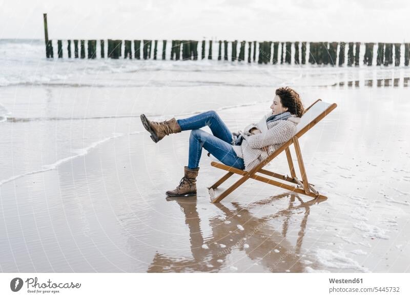 Woman sitting on deckchair on the beach woman females women Seated beaches Adults grown-ups grownups adult people persons human being humans human beings