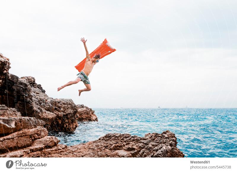 Man with airbed jumping from rock into the sea ocean man men males Leaping water waters body of water Adults grown-ups grownups adult people persons human being