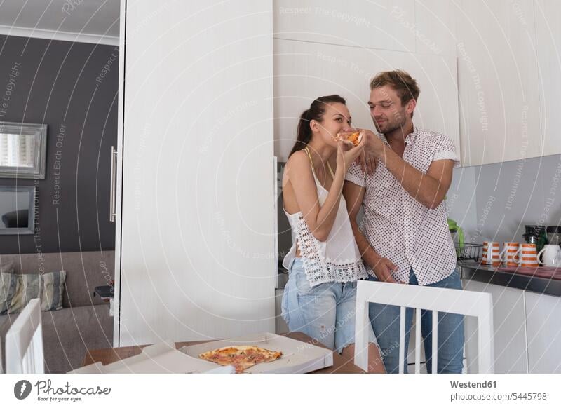 Young couple eating pizza in kitchen Pizza Pizzas domestic kitchen kitchens twosomes partnership couples Food foods food and drink Nutrition Alimentation
