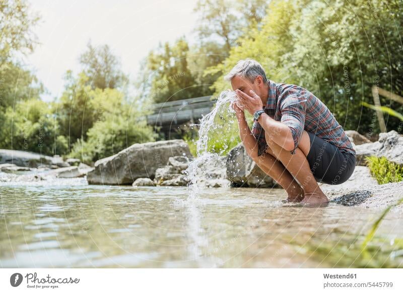 Hiker having a break at the riverbank washing his face hiking hike water man men males Adults grown-ups grownups adult people persons human being humans