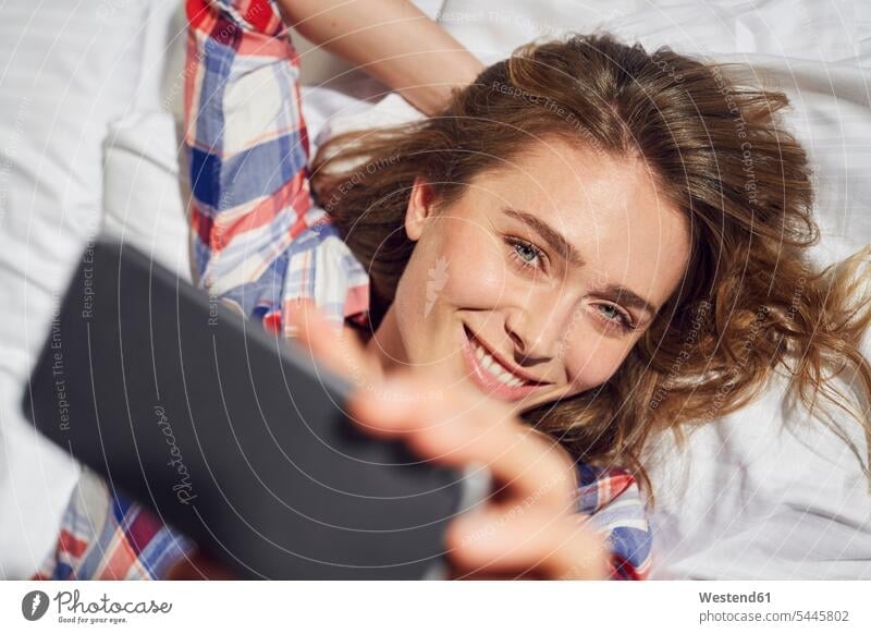 Portrait of laughing woman lying on bed taking selfie with smartphone females women beds portrait portraits Adults grown-ups grownups adult people persons