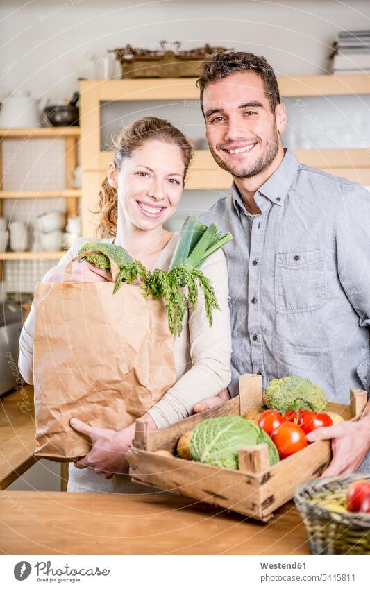 Smiling couple with box of vegetables in kitchen smiling smile twosomes partnership couples Vegetable Vegetables domestic kitchen kitchens people persons