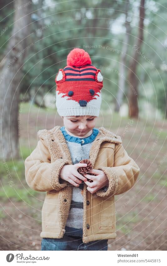 Boy wearing wooly hat holding pine cone in forest Pine Cone Pine Cones Pinecones boy boys males woolly hat Wooly Hat Knit-Hat Knit Hats wool cap child children