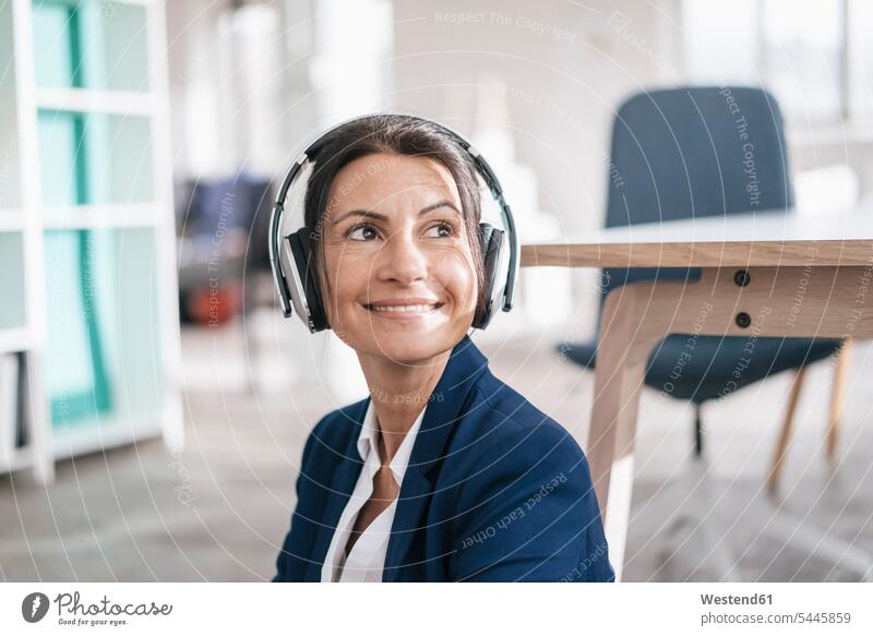 Portrait of smiling businesswoman in a loft listening music with headphones headset portrait portraits females women Adults grown-ups grownups adult people