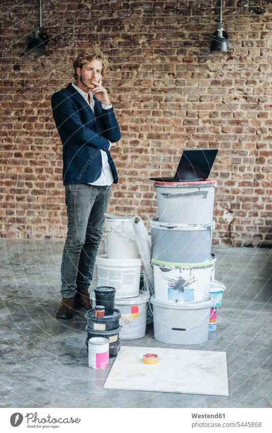 Businessman standing in room with laptop and paint buckets men males moving house move Moving Home thinking Laptop Computers laptops notebook Adults grown-ups