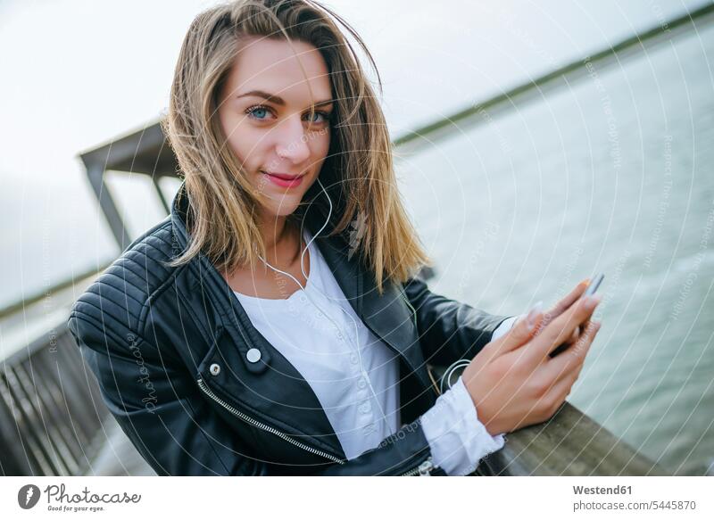 Portrait of smiling young woman with smartphone and earphones on boardwalk portrait portraits females women Adults grown-ups grownups adult people persons