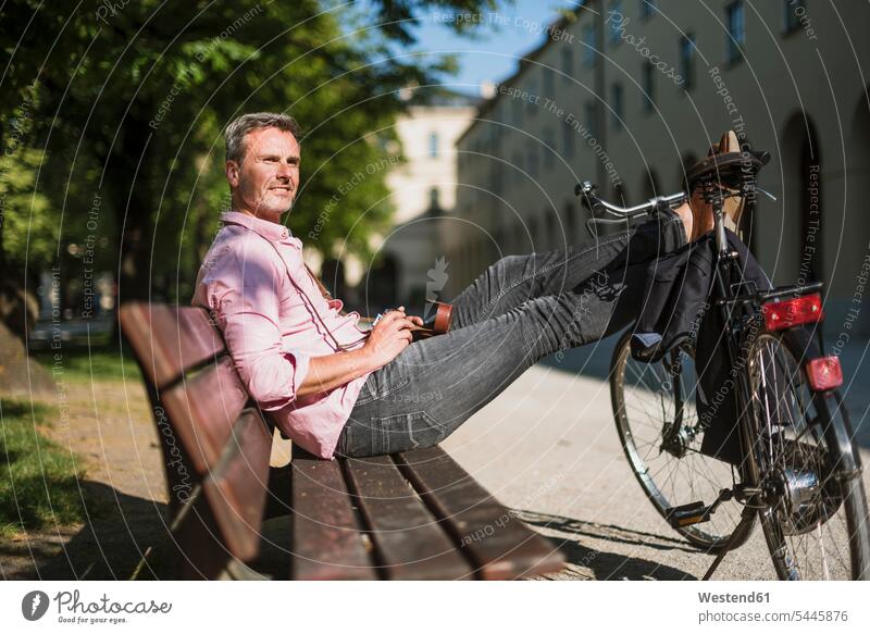 Man with bicycle and old-fashioned camera relaxing on a park bench man men males relaxed relaxation sitting Seated cameras bikes bicycles parks benches city