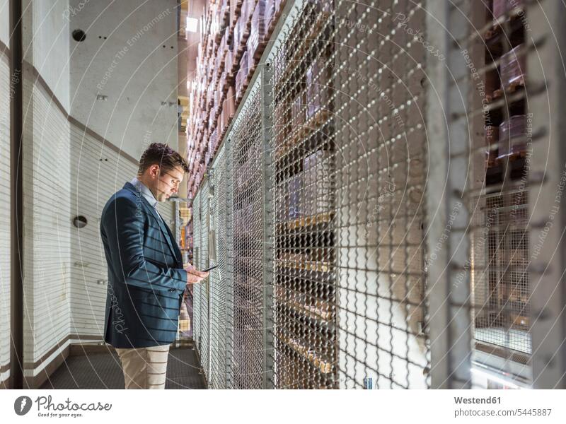 Man in automatized high rack warehouse looking at cell phone man men males working At Work mobile phone mobiles mobile phones Cellphone cell phones Adults